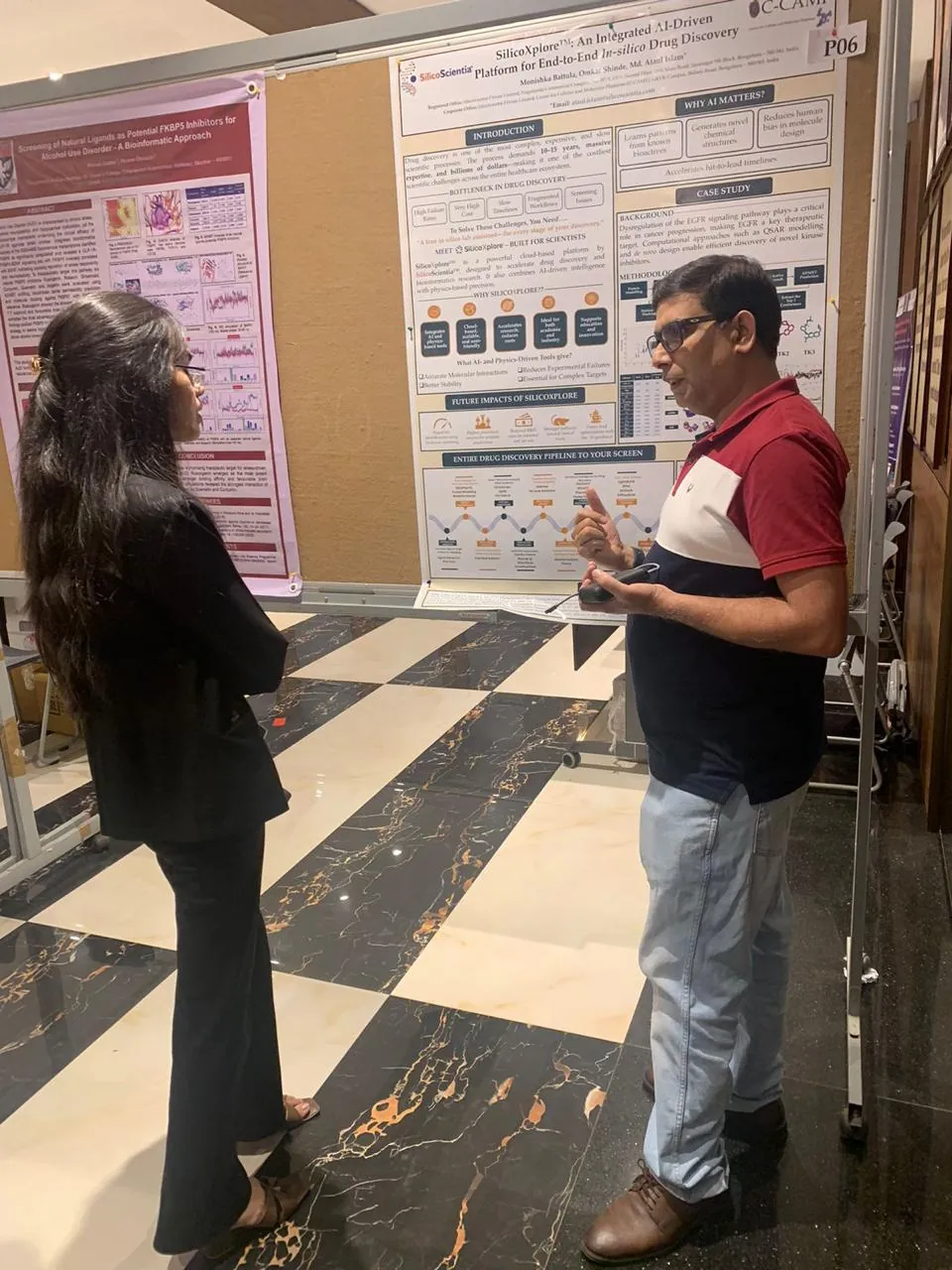 A scientist in a red and navy polo discussing a research poster with a student at a conference