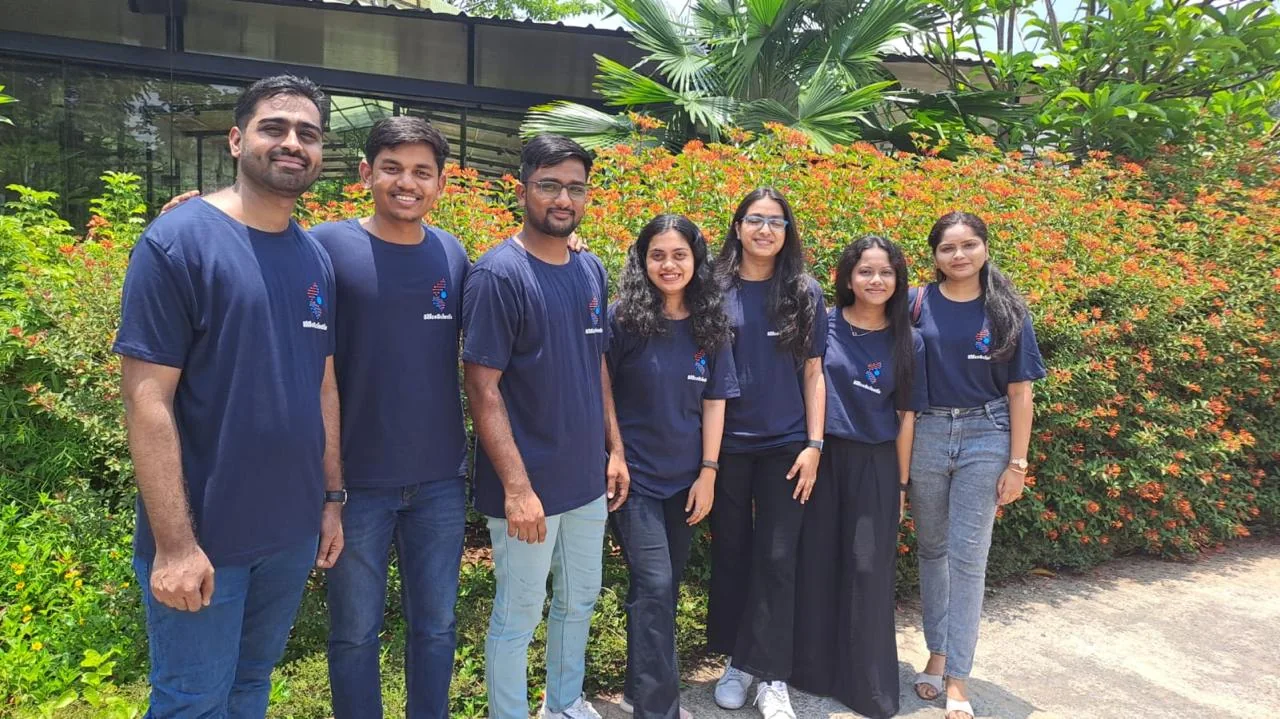 Seven members of the SilicoScientia team in navy company T-shirts, standing together in a garden