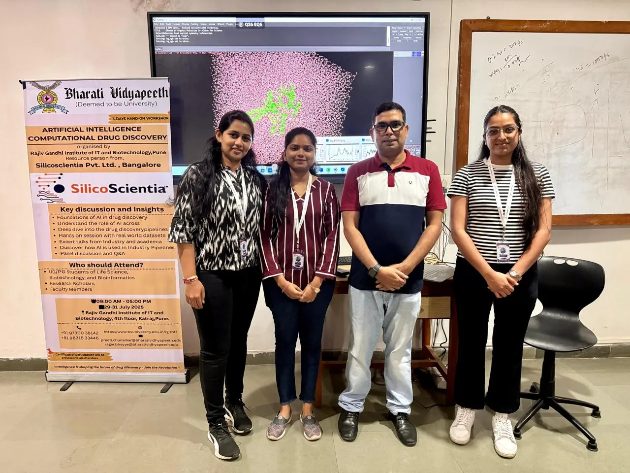 The SilicoScientia team beside the workshop banner in front of a molecular dynamics display