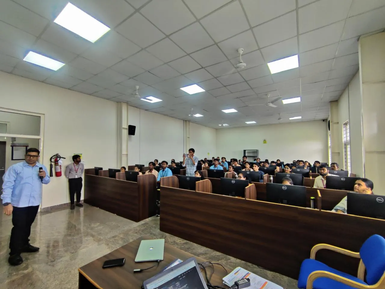 An instructor with a microphone addressing a computer laboratory