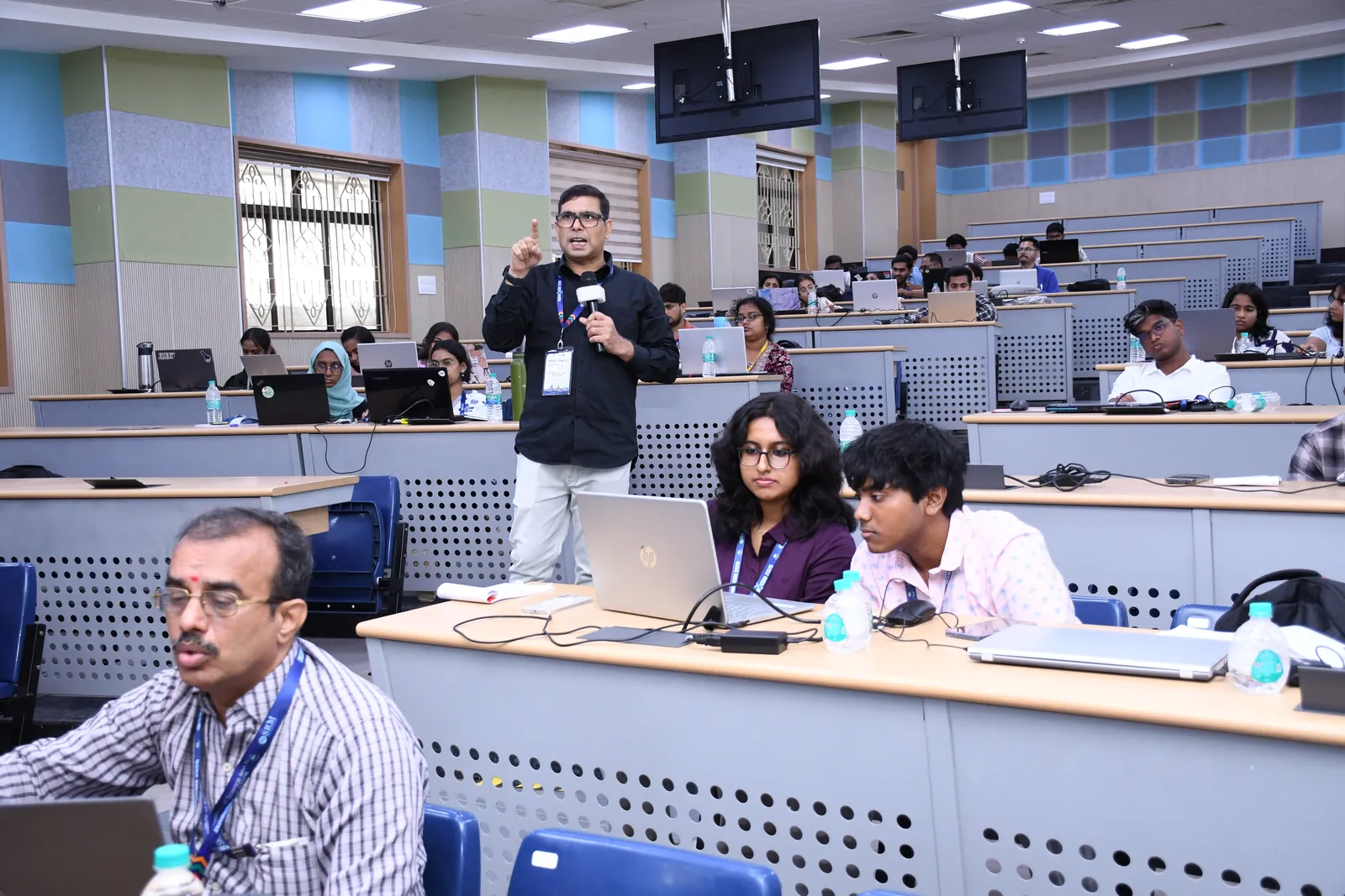 An instructor answering a participant's question in a lecture hall full of laptops